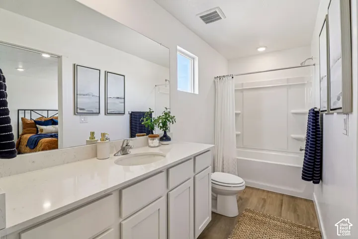 Vanity with an integrated sink and light-toned countertop, white cabinetry with recessed panel doors, wood-finish flooring, and a shower/tub combination with white surround