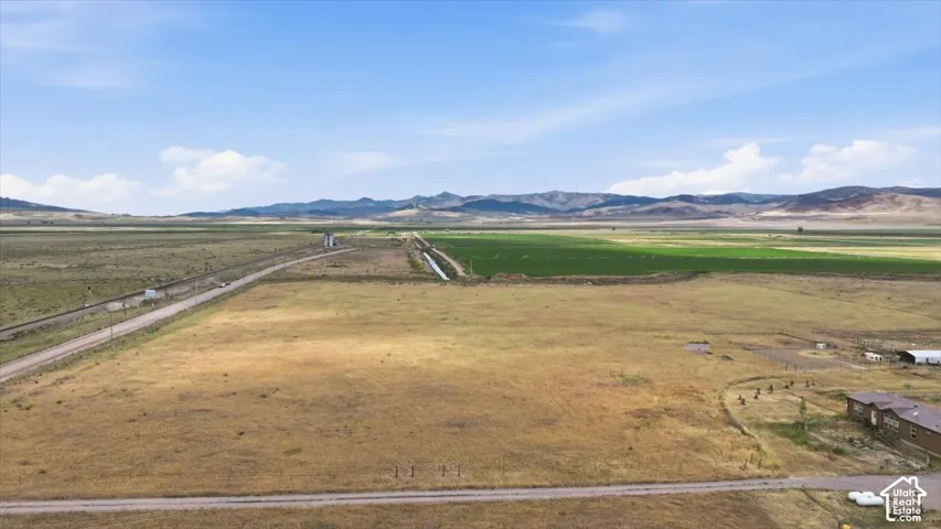 Expansive land featuring a dirt road, cultivated fields, and distant mountains