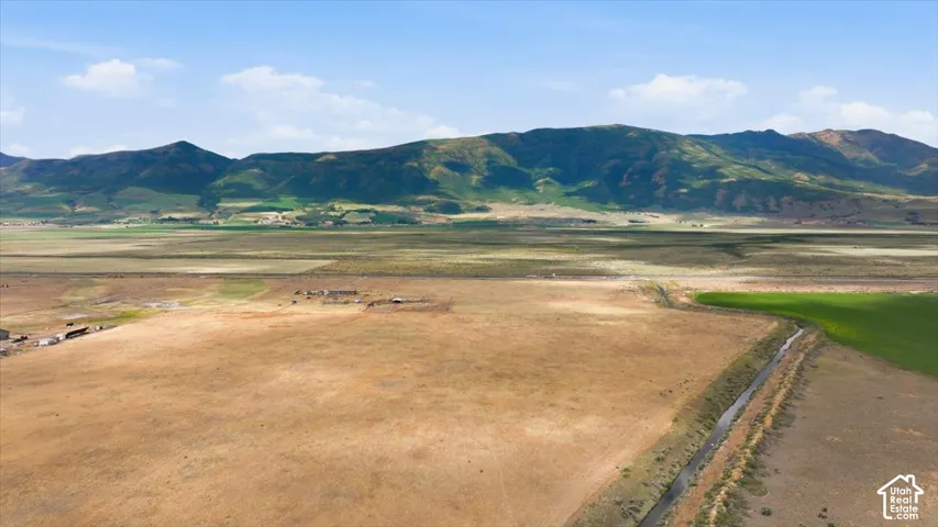 Expansive land parcel with surrounding mountains, an irrigation channel, and visible agricultural cultivation