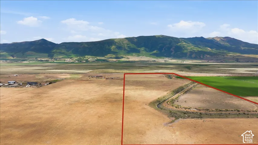 Expansive land parcel featuring open fields, a water channel, and distant mountain backdrops