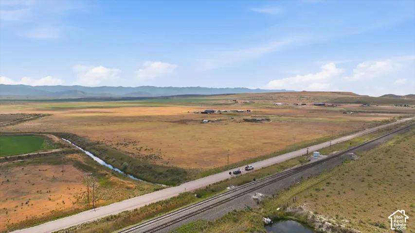 Expansive land featuring a waterway, railway, and distant mountain backdrop