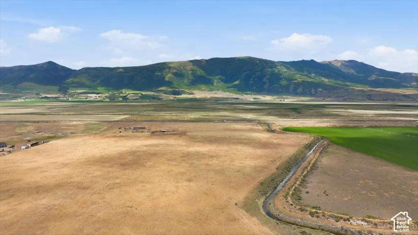 Expansive land parcel featuring a natural water channel, varied terrain with areas of dry and green vegetation, and a mountainous backdrop