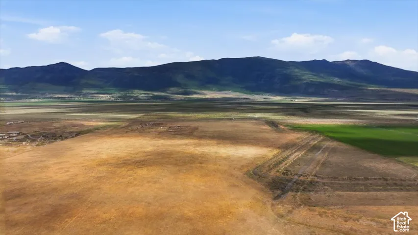 Expansive landscape featuring distant mountains, varying terrain, and partial green fields