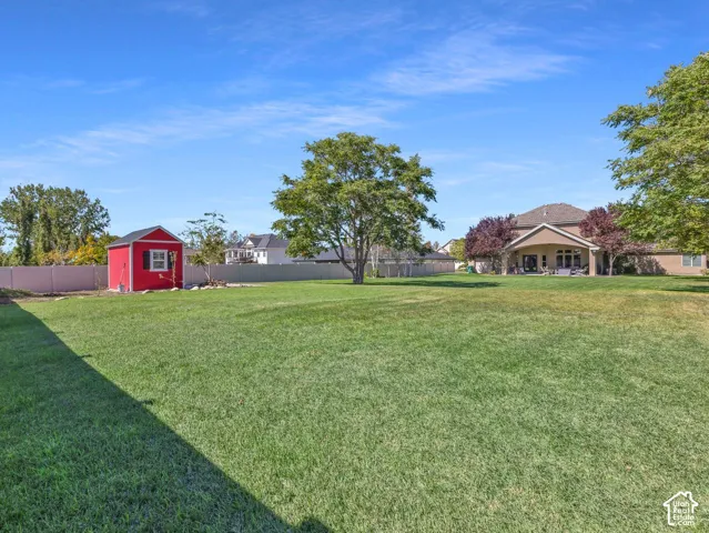 Expansive backyard featuring a red storage shed, full privacy fencing, and mature trees