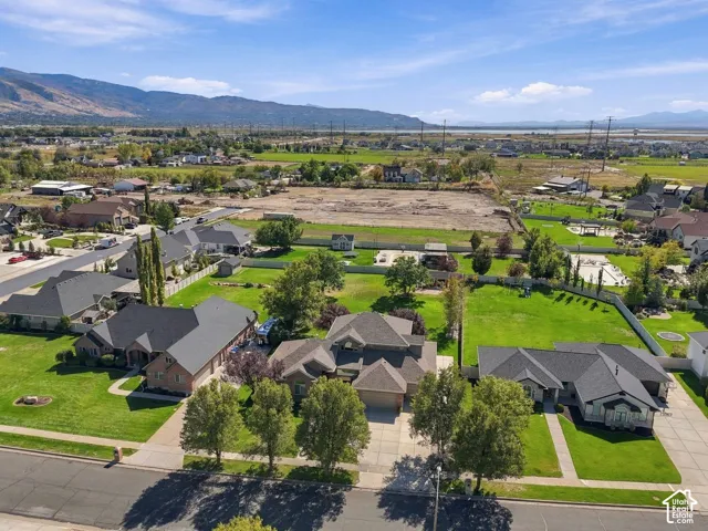 Aerial perspective showcasing a residential street, expansive green lawns, mature trees, and mountainous terrain in the background