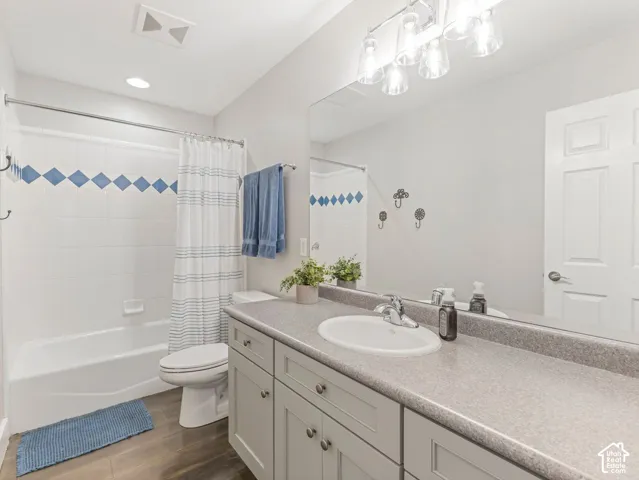 White tiled shower with decorative blue accents, wood-finish flooring, and vanity with built-in sink