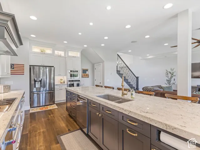 Gourmet kitchen with two-tone cabinetry, stone countertops, stainless steel appliances, and wood-finish flooring