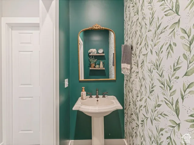 Pedestal sink with brass-finish faucet, framed mirror, and decorative wall covering