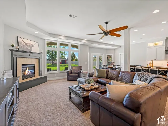 Fireplace with mantel, recessed lighting, ceiling fan, large windows, and carpet flooring