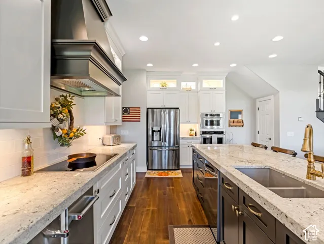 Kitchen featuring an expansive island with an undermount sink, recessed lighting, wood-finish flooring, white cabinetry, and stainless steel appliances
