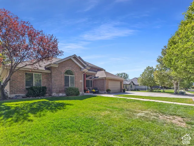 Brick exterior with arched window, attached garage, concrete driveway, and mature landscaping