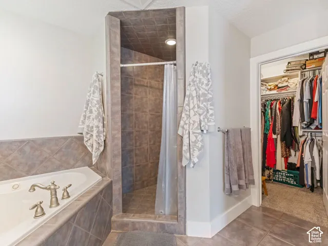 Tiled shower enclosure with recessed lighting, a corner soaking tub with deck-mounted fixtures, and a walk-in closet with built-in shelving