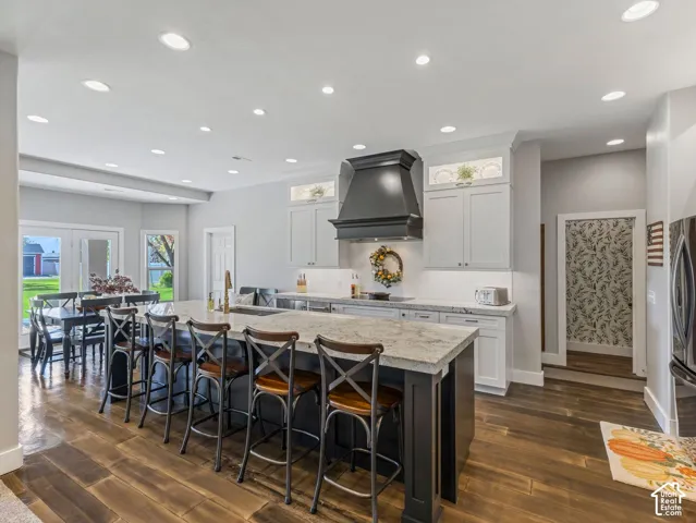 Spacious kitchen with a large central island, recessed lighting, wood-finish flooring, white cabinetry, and granite countertops