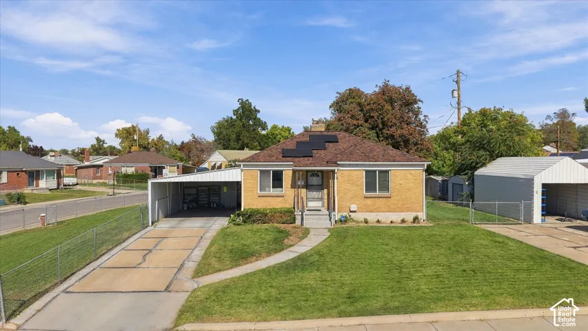 Brick exterior, attached carport, solar panel array, manicured lawn, and paved driveway
