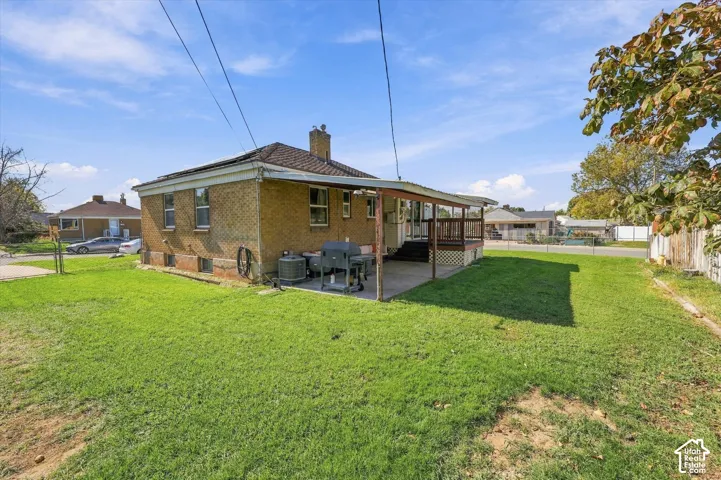 Brick exterior with a covered patio, wood deck, and a spacious grassy yard