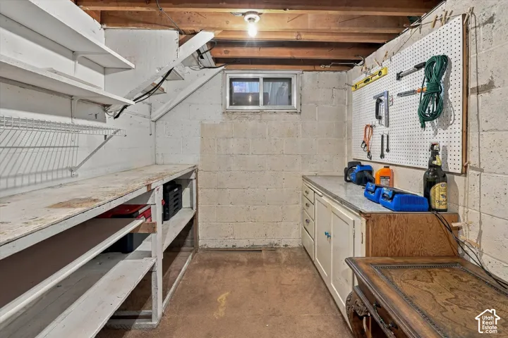Built-in workbench with shelving, exposed wood ceiling joists, built-in cabinetry, and a utility window