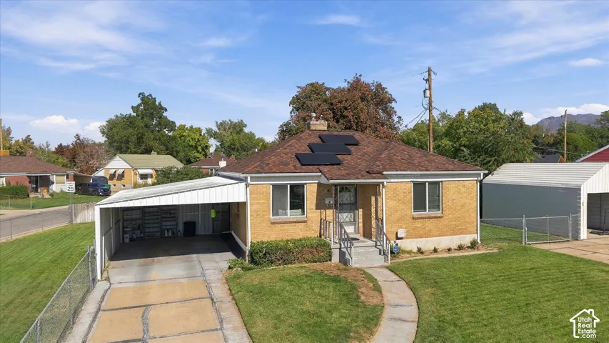Brick exterior with a brown shingle roof, solar panel installation, paved driveway, and covered carport