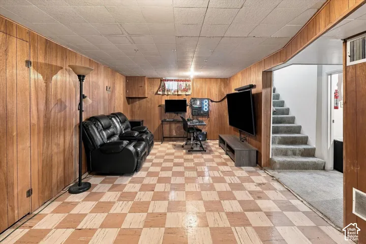 Wood-panel walls, checkered flooring, drop ceiling, and carpeted stairs