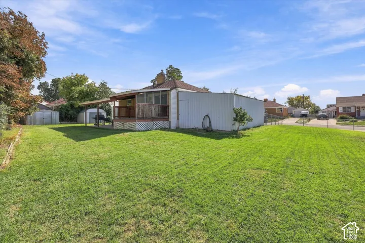 Expansive green lawn, covered wooden deck, screened-in porch, additional storage shed, and adjacent carport