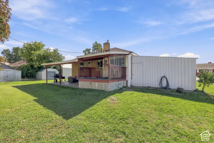 Expansive grassy yard featuring a covered patio, raised deck, and a white shed structure