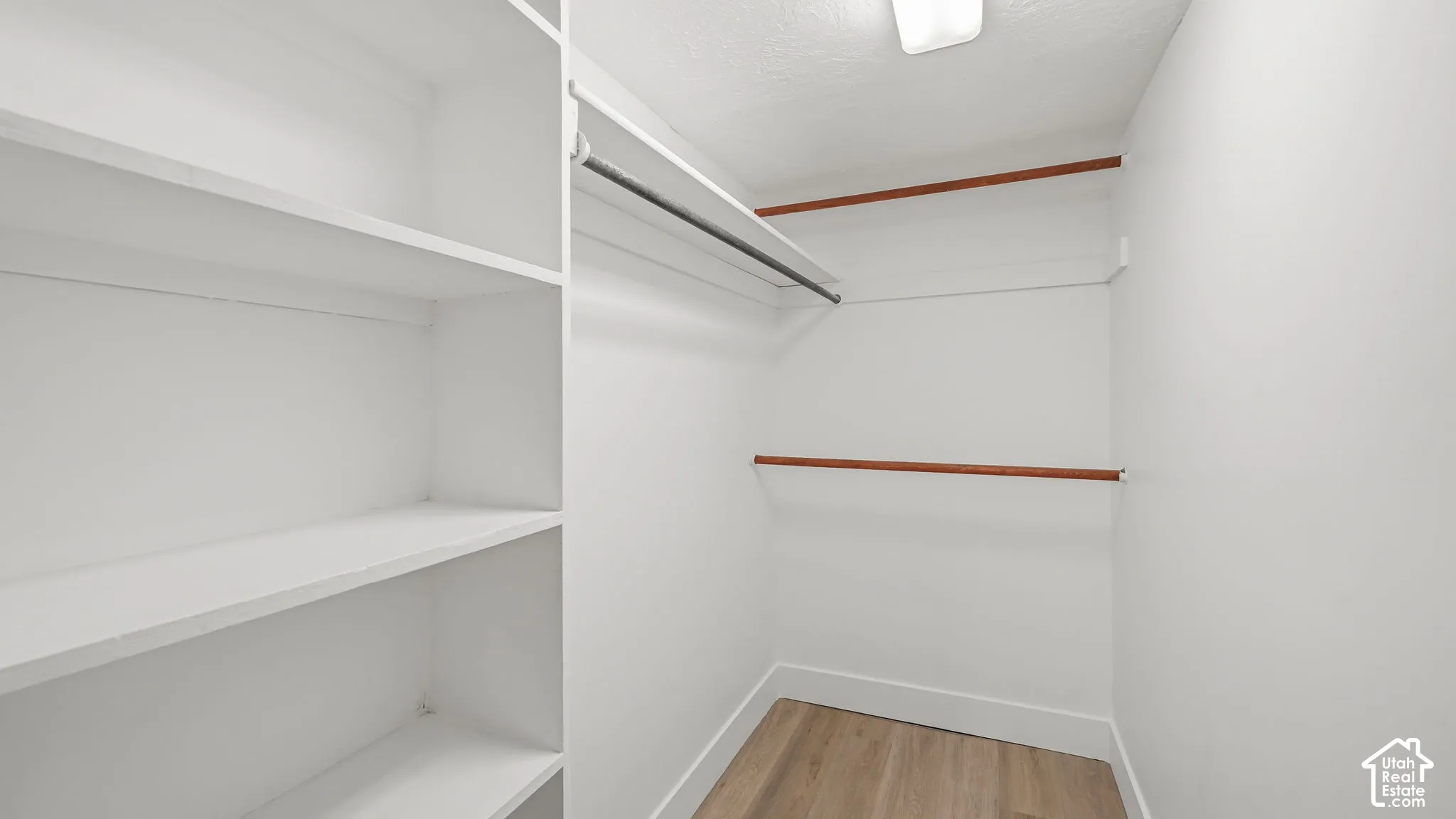 Walk-in closet featuring built-in shelving, multiple hanging rods, and wood-finish flooring