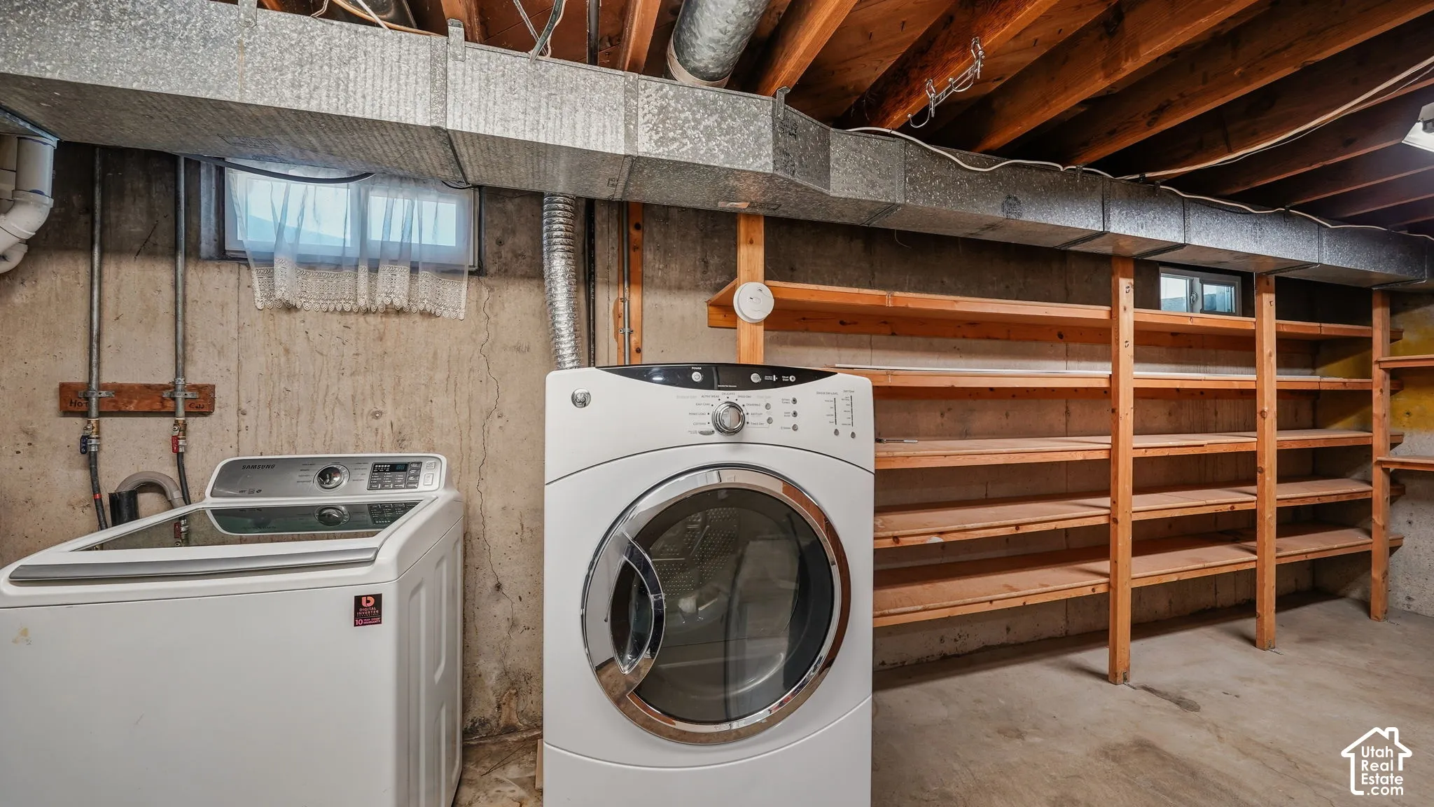 Laundry area featuring built-in wooden shelving, concrete flooring, and exposed ceiling beams
