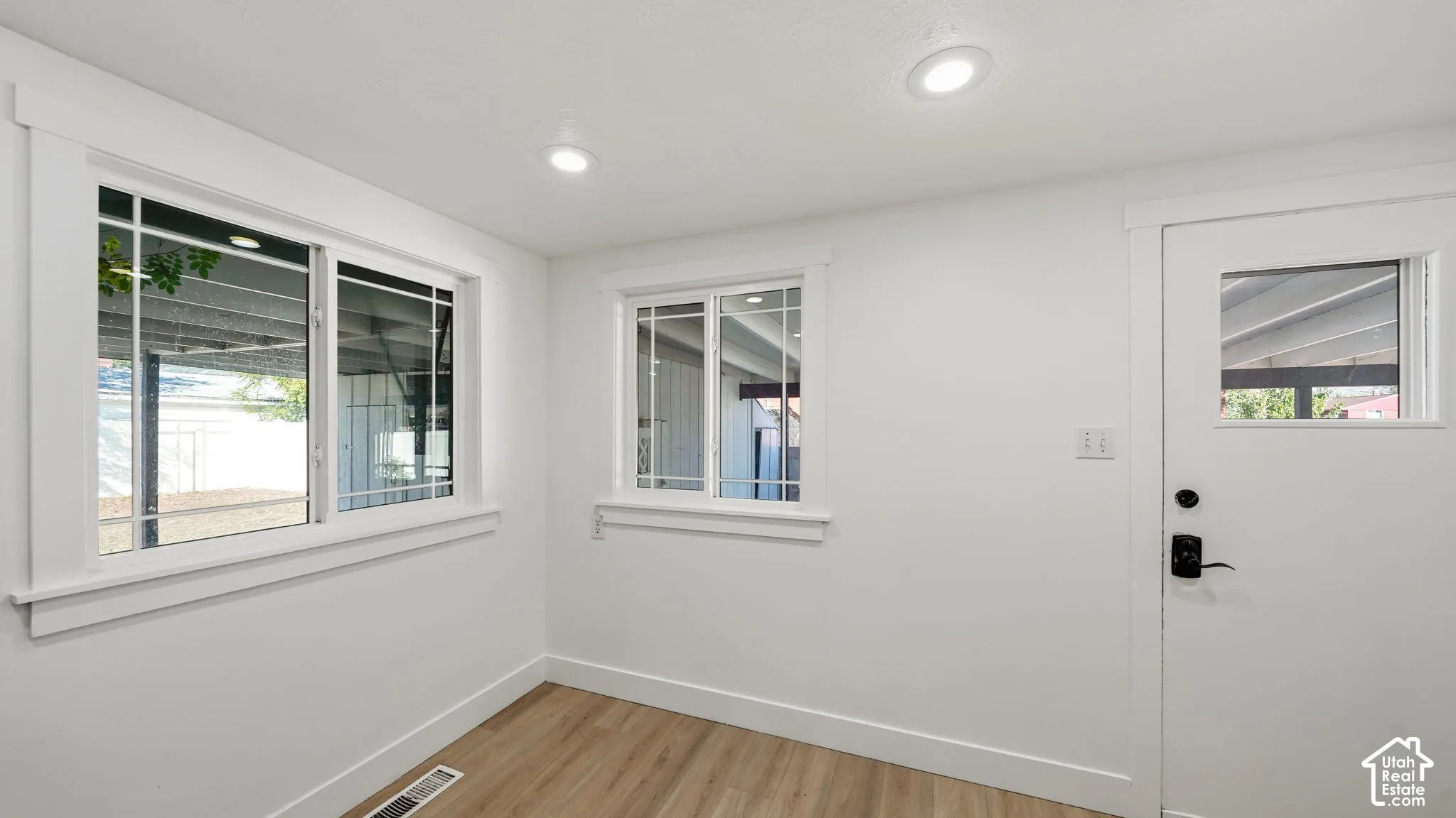 Recessed ceiling lighting, multiple windows with white trim, a white door with a window pane, and wood-finish flooring
