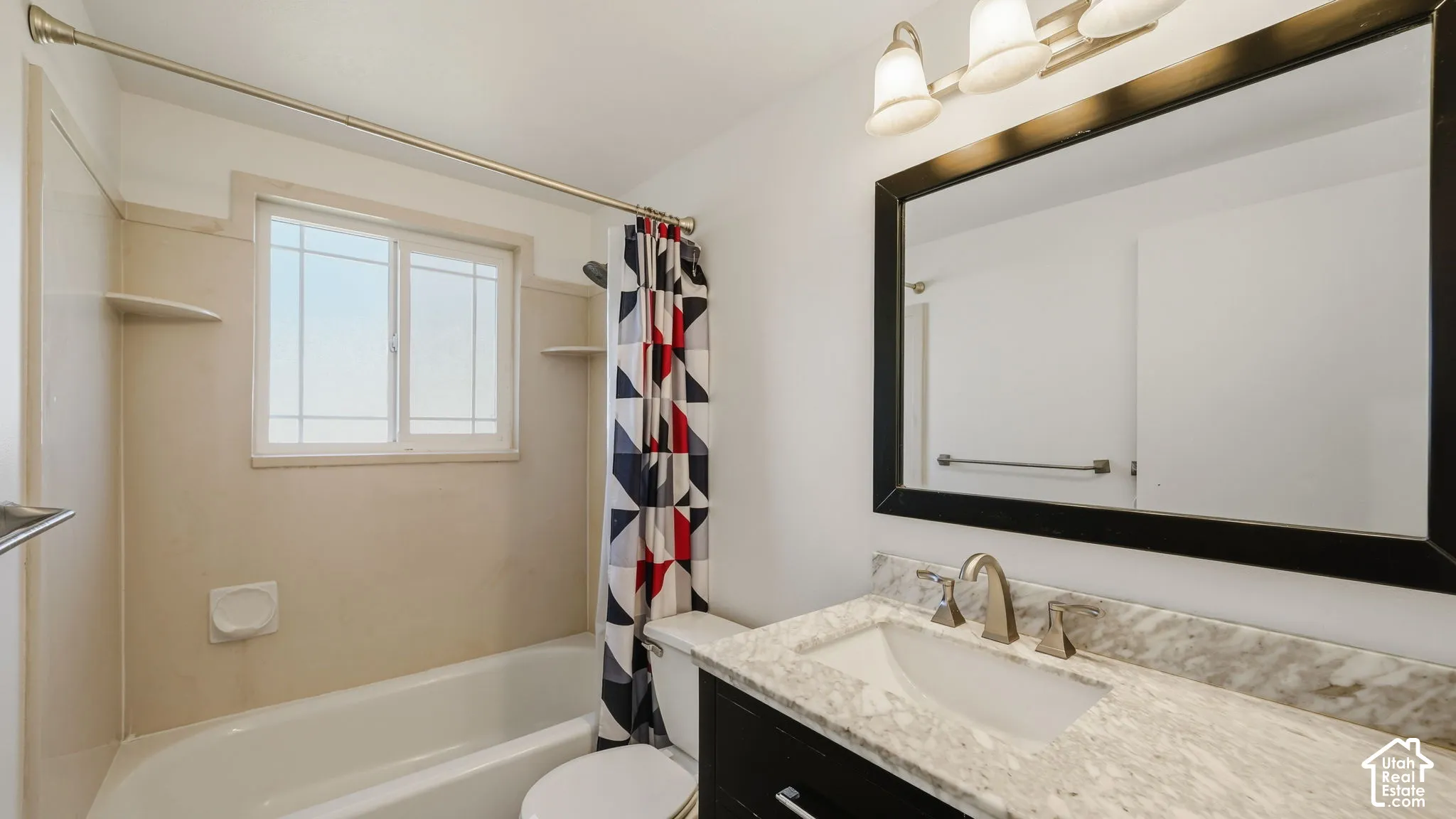 Bathroom featuring a white bathtub, vanity with a stone countertop, framed mirror, and window