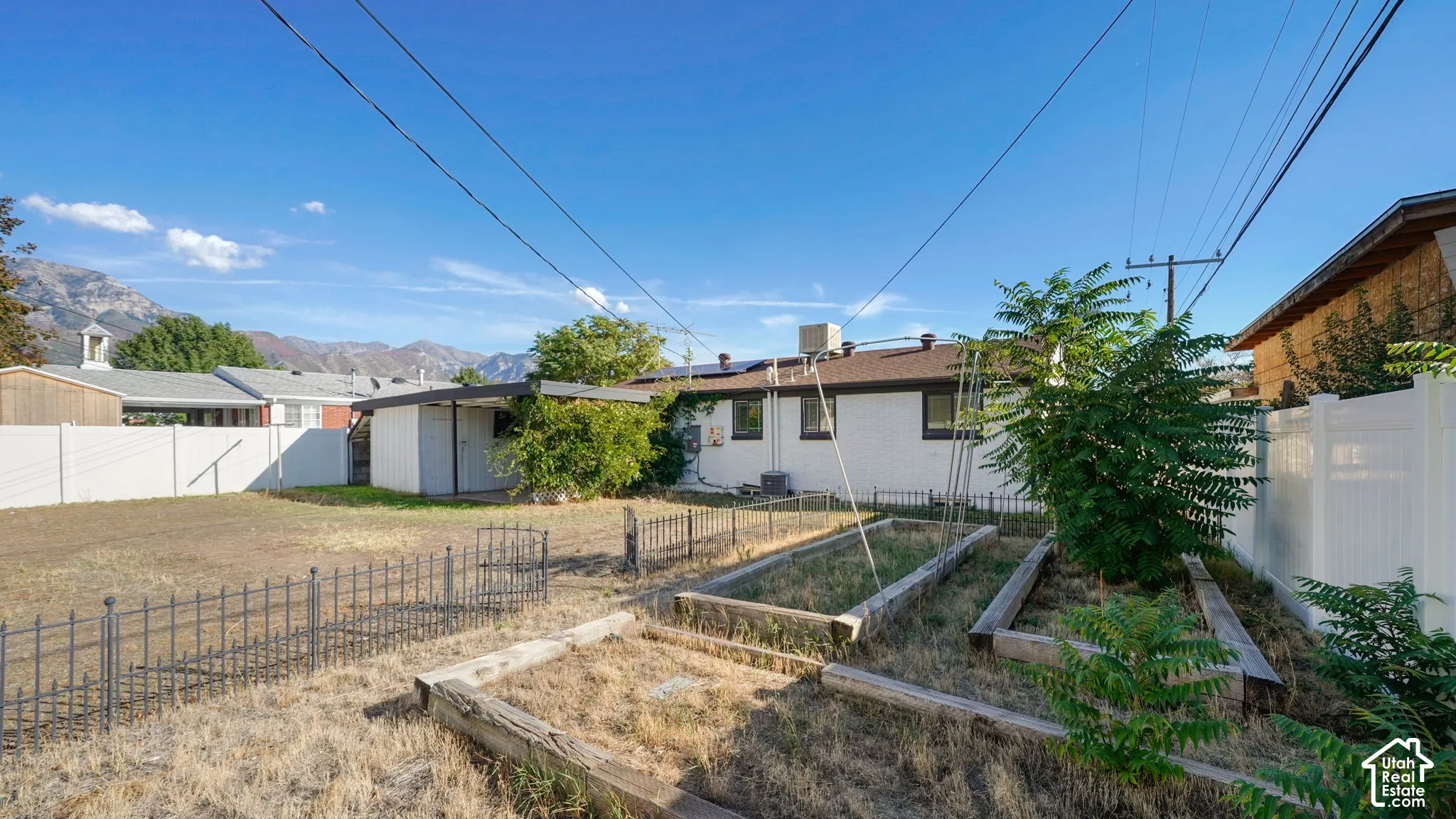 Expansive yard with mountain scenery, white privacy fencing, raised garden beds, and a detached shed structure
