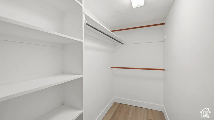 Walk-in closet featuring built-in shelving, multiple hanging rods, and wood-finish flooring