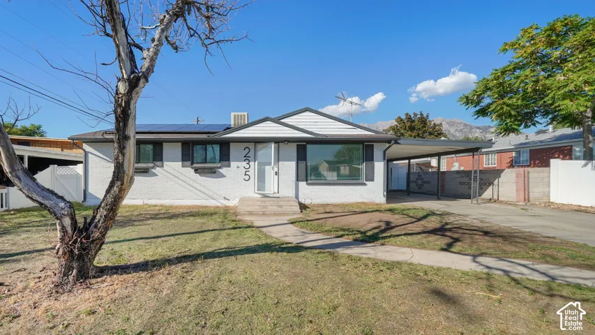 White exterior with dark trim accents, covered carport, concrete driveway, and established front yard