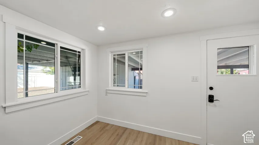 Recessed ceiling lighting, multiple windows with white trim, a white door with a window pane, and wood-finish flooring