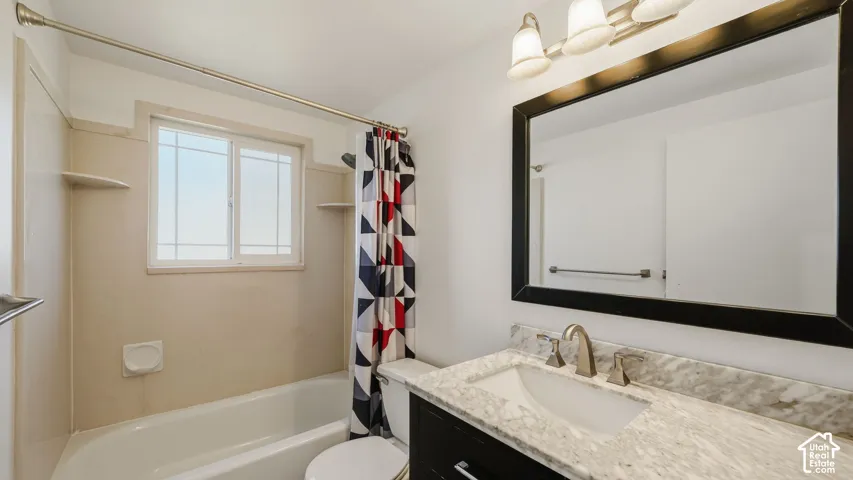 Bathroom featuring a white bathtub, vanity with a stone countertop, framed mirror, and window
