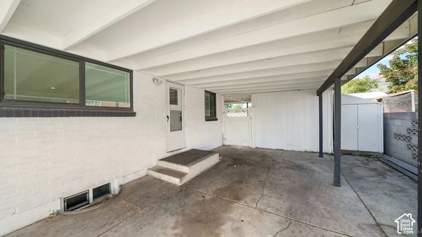 Covered concrete patio with white painted brick siding, black framed windows, and a built-in storage shed