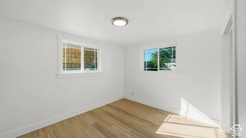 Wood-finish flooring with white baseboards, white walls, and two windows with white trim