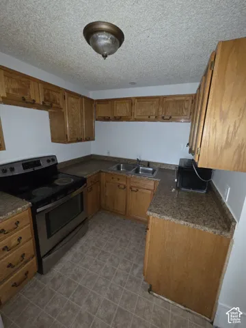 Kitchen featuring wood-finish cabinetry, stone-look countertops, stainless steel range, and a dual basin sink