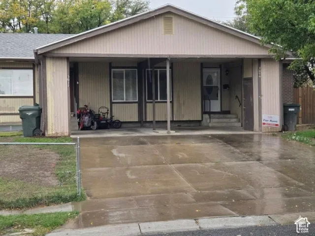 Single-story exterior with a covered entry, concrete driveway, and a chain-link fence