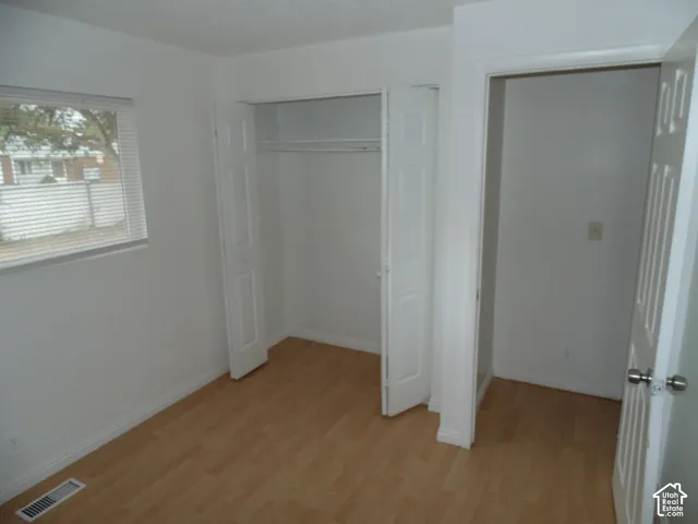 Wood-finish flooring with white trim and a window featuring horizontal blinds