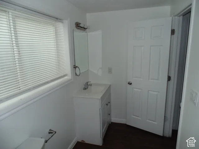 Vanity with integrated sink, wall-mounted mirror with overhead lighting, six-panel interior door, and wood-finish flooring