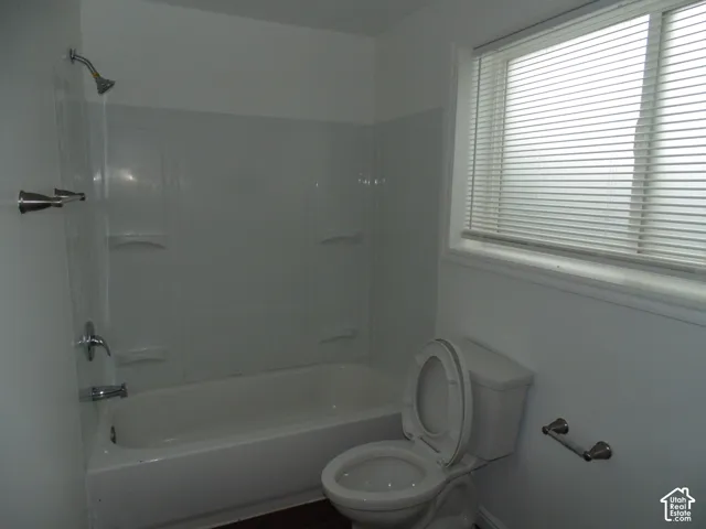 White bathtub and shower combination with chrome fixtures, a toilet, and a window with blinds