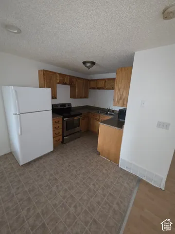 Kitchen featuring wood cabinetry, a stainless steel range, a white refrigerator, and patterned floor tile