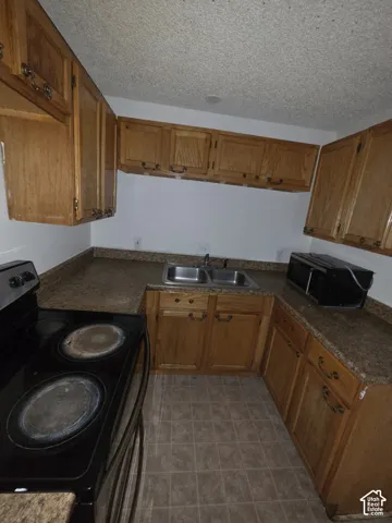 U-shaped kitchen layout featuring wood cabinetry, laminate countertops, a double basin stainless steel sink, and tile flooring