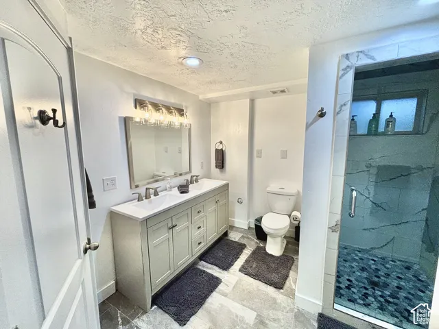 Dual vanity with undermount sinks, frameless shower with patterned tile, recessed ceiling lighting, textured ceiling finish, and contemporary wall-mounted light fixture