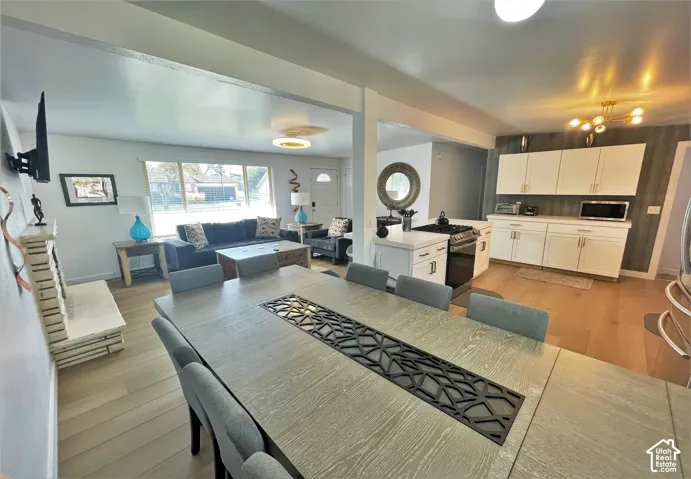 Open-concept living area with wood-finish flooring, a contemporary dining table, a kitchen with white cabinetry, and a gas range