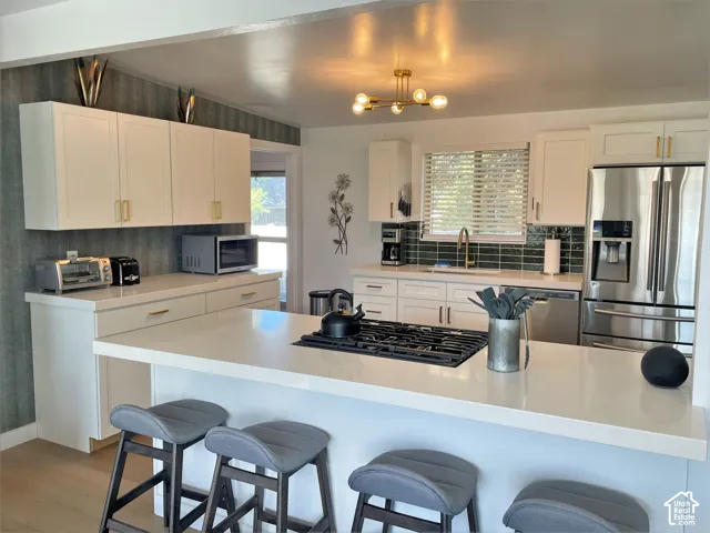 White cabinetry with gold-tone hardware, stainless steel appliances, a center island with a gas cooktop, and subway tile backsplash