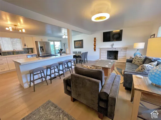Open-concept living area featuring wood-finish flooring, a kitchen island with seating, a fireplace with a stone surround, and stainless steel appliances