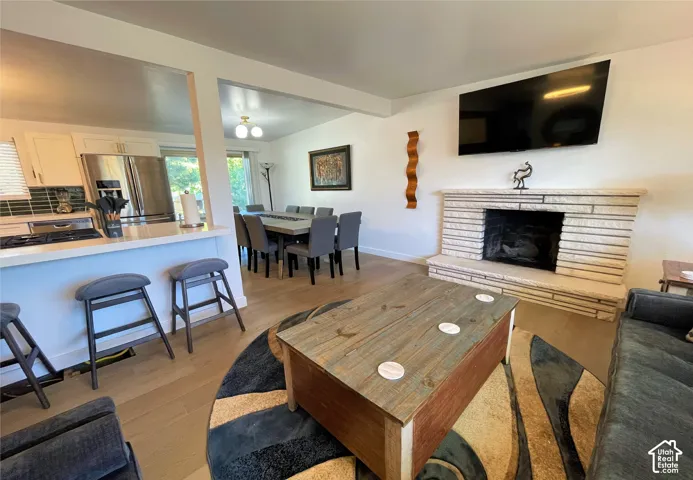 Open concept living area featuring wood-finish flooring, a stone-clad fireplace, a breakfast bar, stainless steel appliances, and built-in cabinetry