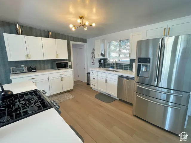 Contemporary kitchen featuring white cabinetry, light wood-finish flooring, stainless steel appliances, a tile backsplash, and a modern light fixture