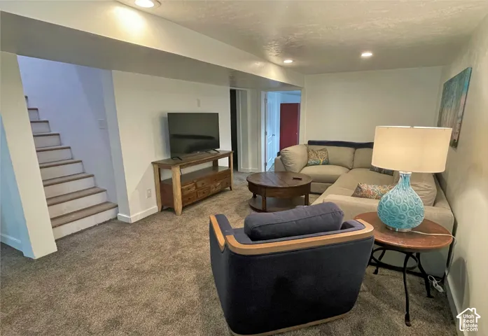 Recessed lighting illuminates this living space with carpet flooring and a built-in staircase