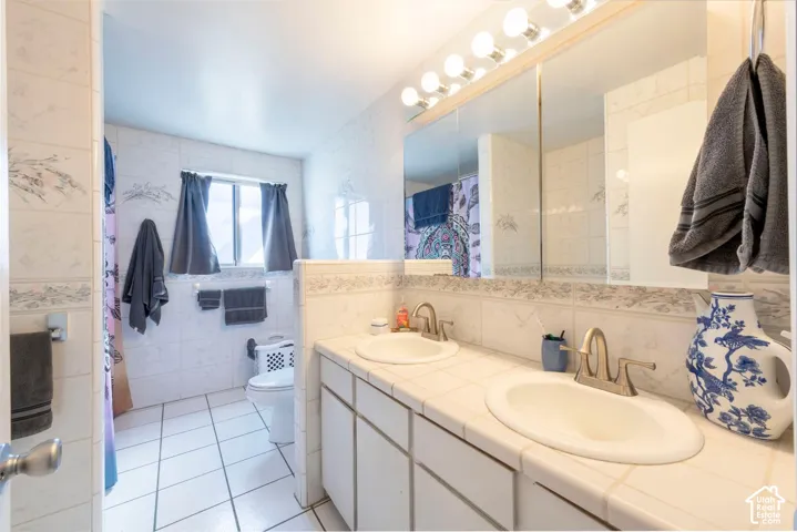 Dual vanity with integrated sinks, tiled countertop, large mirror, and overhead strip lighting